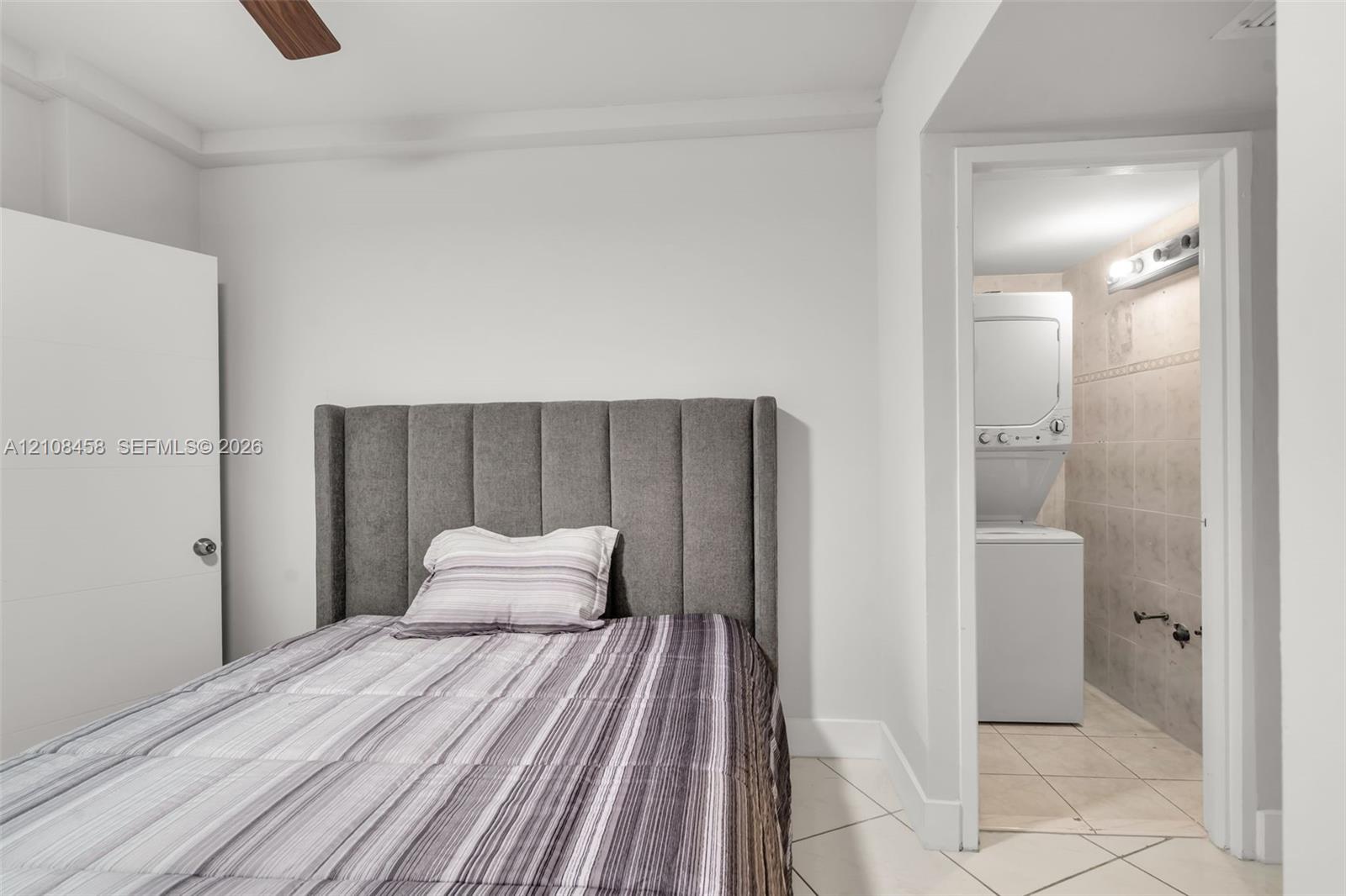 Interior space featuring white walls, tiled flooring, ceiling fan, and a dedicated laundry area with stacked washer and dryer unit