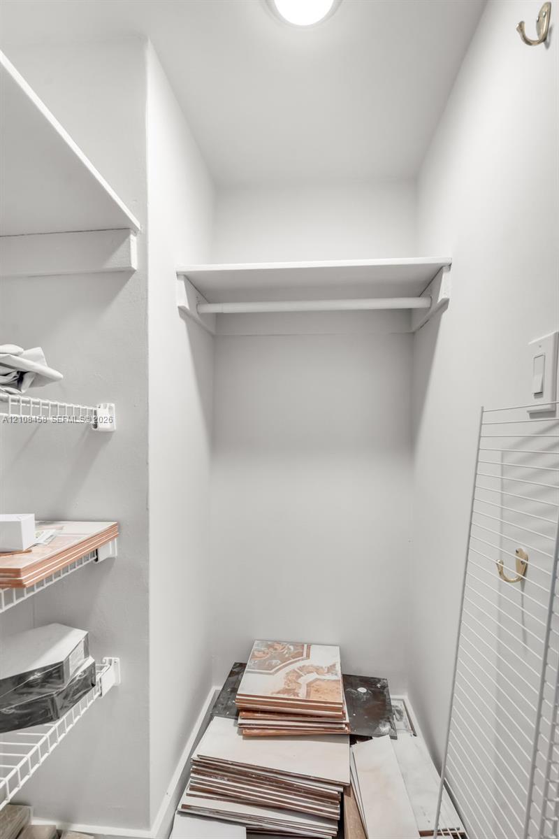 Storage closet featuring white wire shelving, a high-mounted clothes rod, and wall-mounted metal hooks