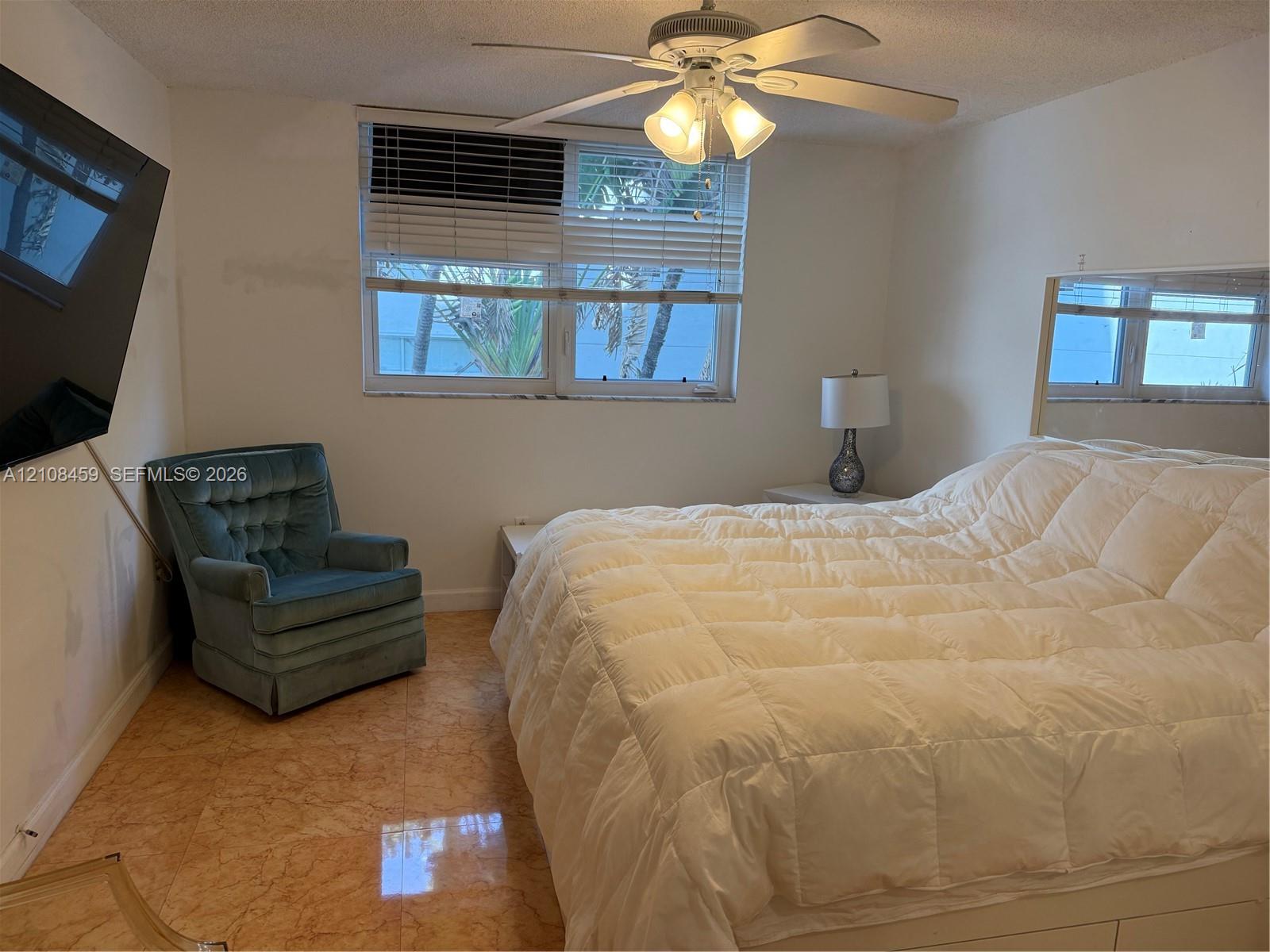 Polished stone flooring, ceiling-mounted fan with integrated light fixture, large-format wall mirror, and window with blinds Polished stone flooring, ceiling-mounted fan with integrated light fixture, large-format wall mirror, and window with blinds