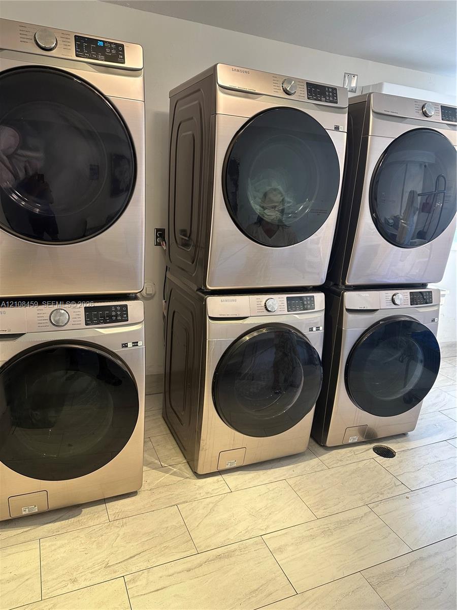 Laundry area featuring five stacked front-load washers and dryers with metallic finishes and light-toned tile flooring