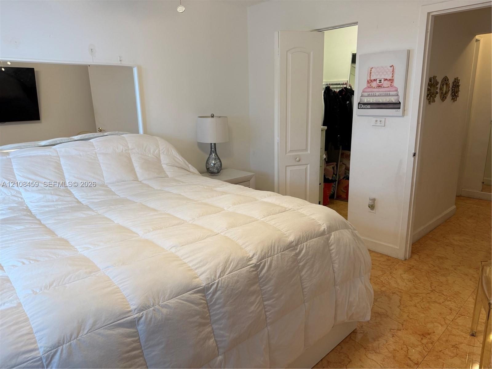Bedroom featuring a large wall-mounted mirror, neutral interior paint, stone-finish tile flooring, and a walk-in closet with an arched two-panel door Bedroom featuring a large wall-mounted mirror, neutral interior paint, stone-finish tile flooring, and a walk-in closet with an arched two-panel door
