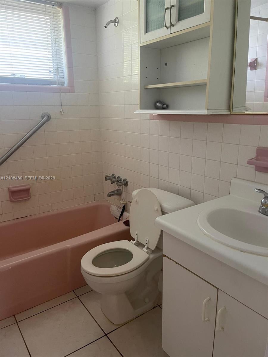 Bathroom featuring a porcelain bathtub, white tile wall surround, built-in medicine cabinet with shelving, vanity with a white countertop, and tiled flooring Bathroom featuring a porcelain bathtub, white tile wall surround, built-in medicine cabinet with shelving, vanity with a white countertop, and tiled flooring