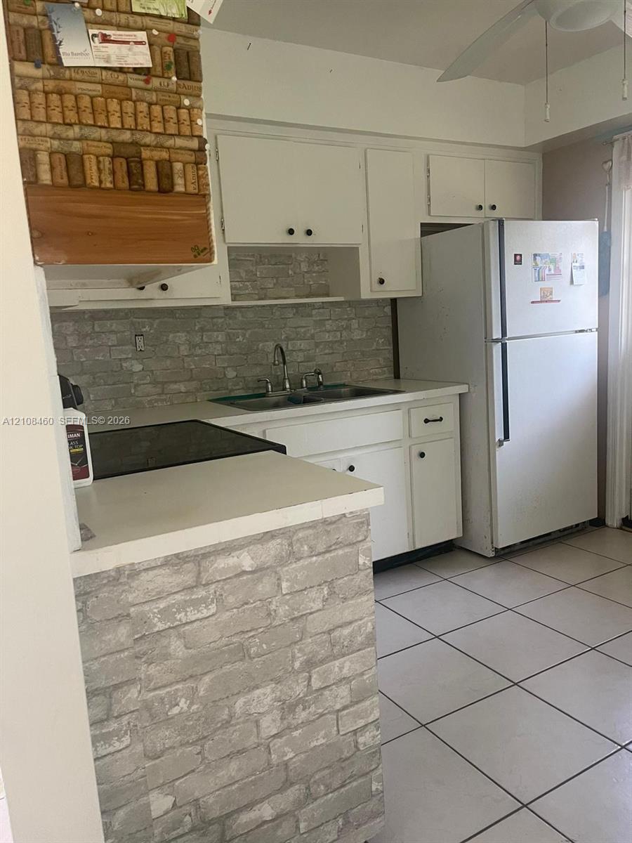 Kitchen featuring white cabinetry, brick-pattern backsplash and peninsula base, ceramic tile flooring, and a stainless steel double-basin sink Kitchen featuring white cabinetry, brick-pattern backsplash and peninsula base, ceramic tile flooring, and a stainless steel double-basin sink