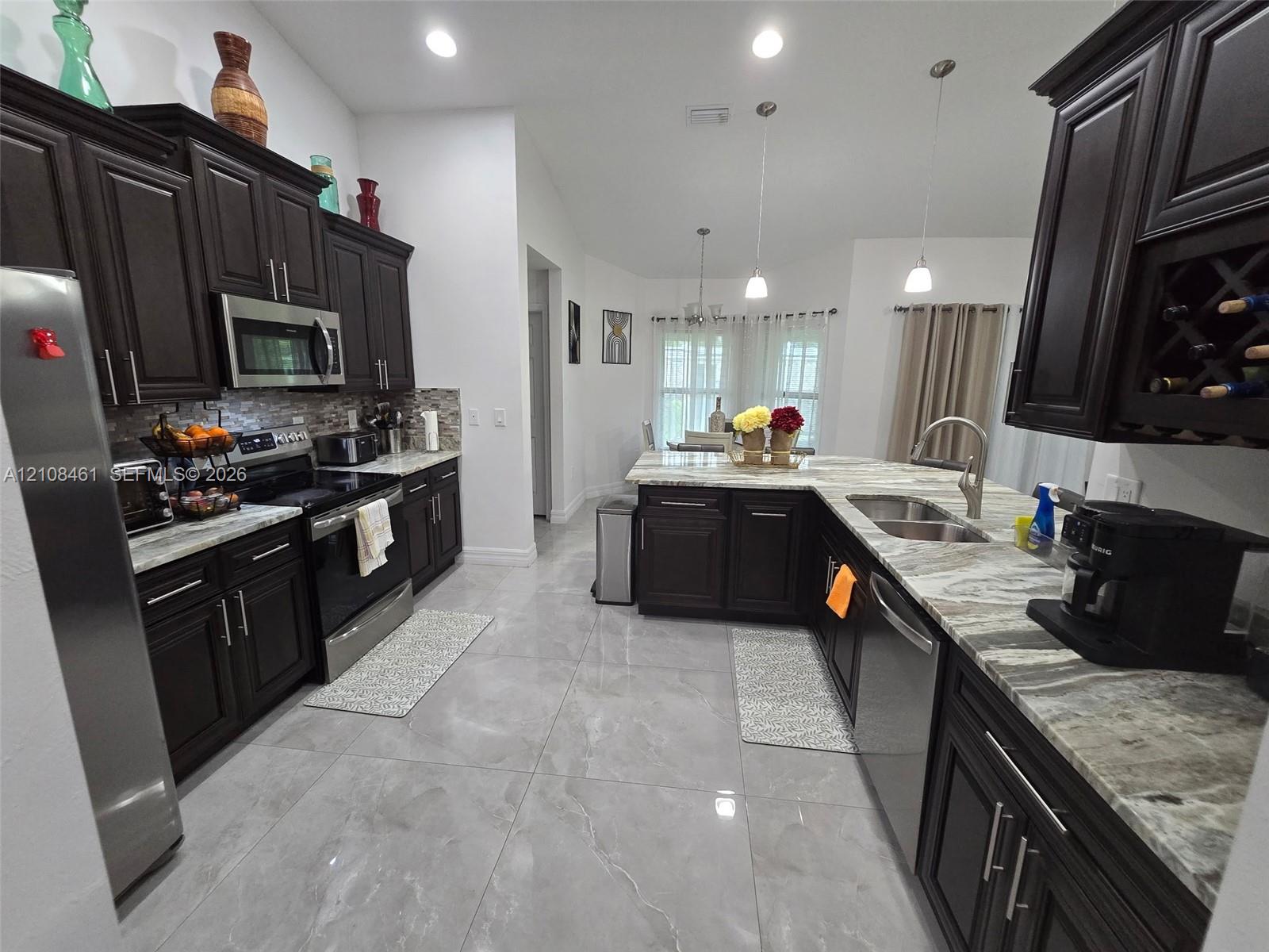 Kitchen featuring dark wood cabinetry, integrated wine storage, natural stone countertops, tile flooring, and stainless steel appliances