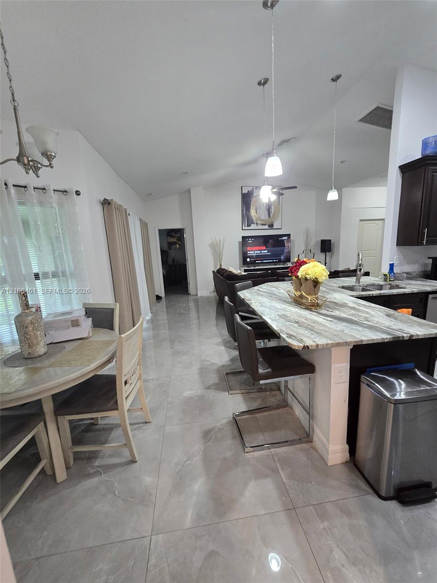 Open-concept area featuring large-format polished tile flooring, vaulted ceilings, and a kitchen island with stone-patterned countertop
