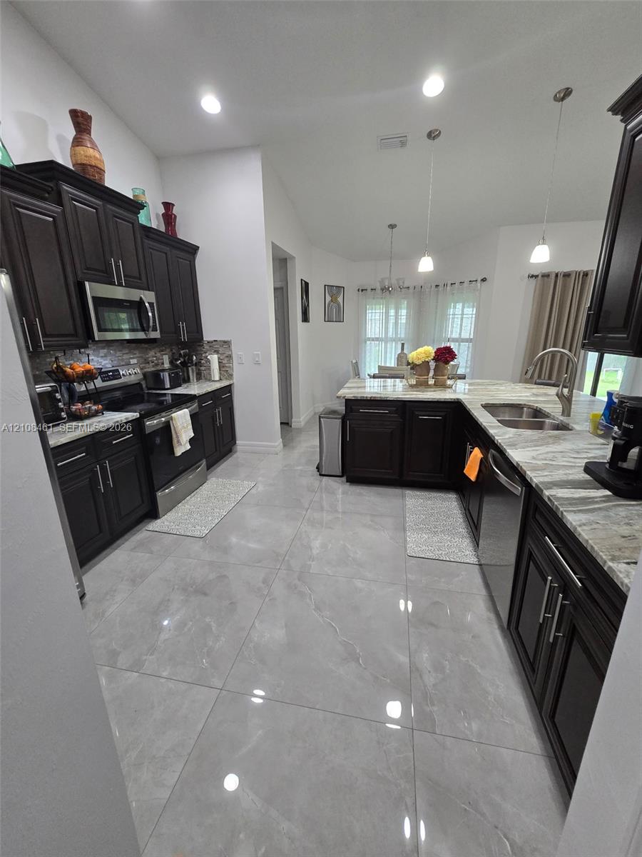 Kitchen featuring dark wood cabinetry, large-format polished tile flooring, stone-finish countertops, stainless steel appliances, and pendant lighting
