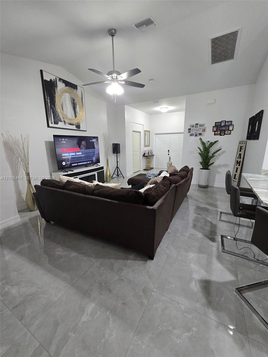High-ceiling living area featuring large-format polished tile flooring, a brushed nickel ceiling fan with integrated lighting, and neutral wall tones