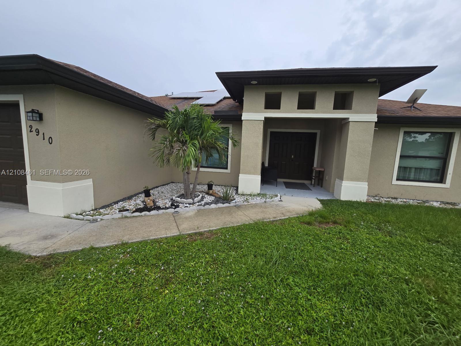 Stucco exterior with decorative columns, integrated solar panels, recessed entry lighting, and low-maintenance rock garden landscaping