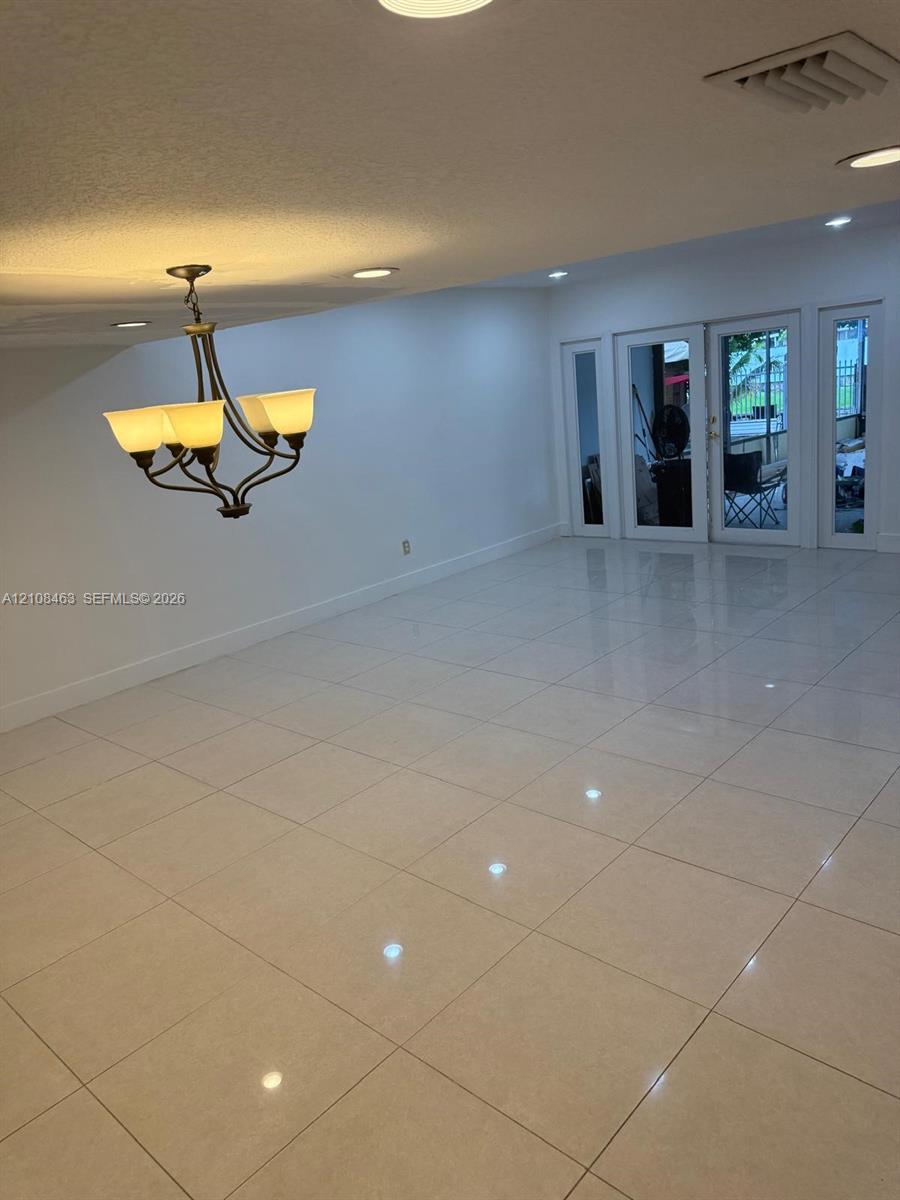 Large-format tile flooring, recessed ceiling lighting, and a multi-arm chandelier with glass shades, featuring double glass-paneled exterior doors with flanking sidelights Large-format tile flooring, recessed ceiling lighting, and a multi-arm chandelier with glass shades, featuring double glass-paneled exterior doors with flanking sidelights