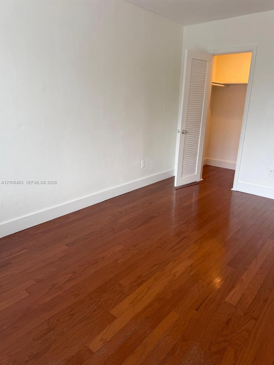 Room featuring wood-finish flooring, neutral wall paint, and a built-in closet with a louvered door