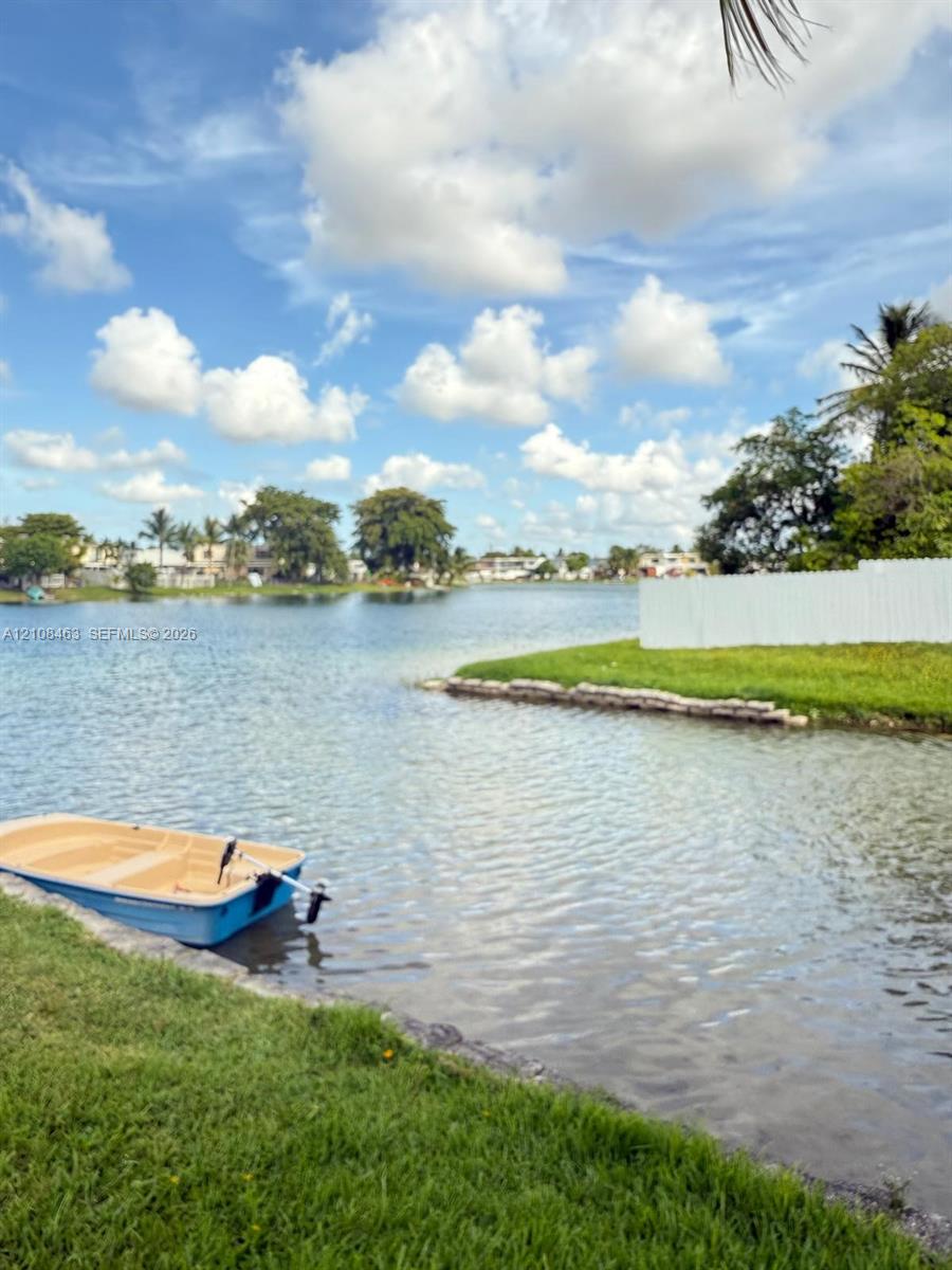 Waterfront property featuring a manicured lawn, stone-lined bulkhead, and white perimeter fencing