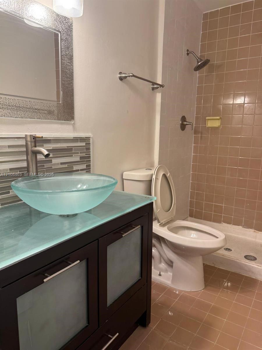 Dark wood-finish vanity with frosted glass cabinet panels, glass countertop, vessel sink, and metallic faucet hardware complemented by a glass tile backsplash and tiled shower surround