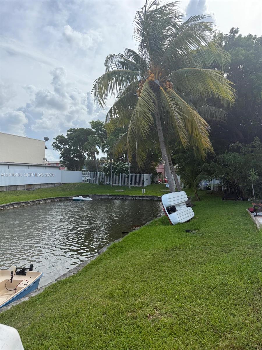 Waterfront backyard featuring a manicured lawn, stone-lined canal bulkhead, and mature palm tree
