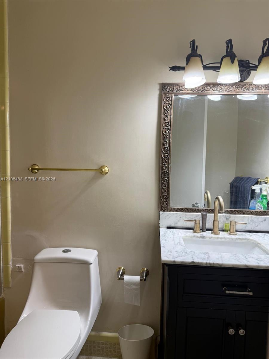 Bathroom vanity featuring a dark-finish base, stone countertop with integrated basin, three-light fixture, decorative framed mirror, and metallic hardware accents Bathroom vanity featuring a dark-finish base, stone countertop with integrated basin, three-light fixture, decorative framed mirror, and metallic hardware accents