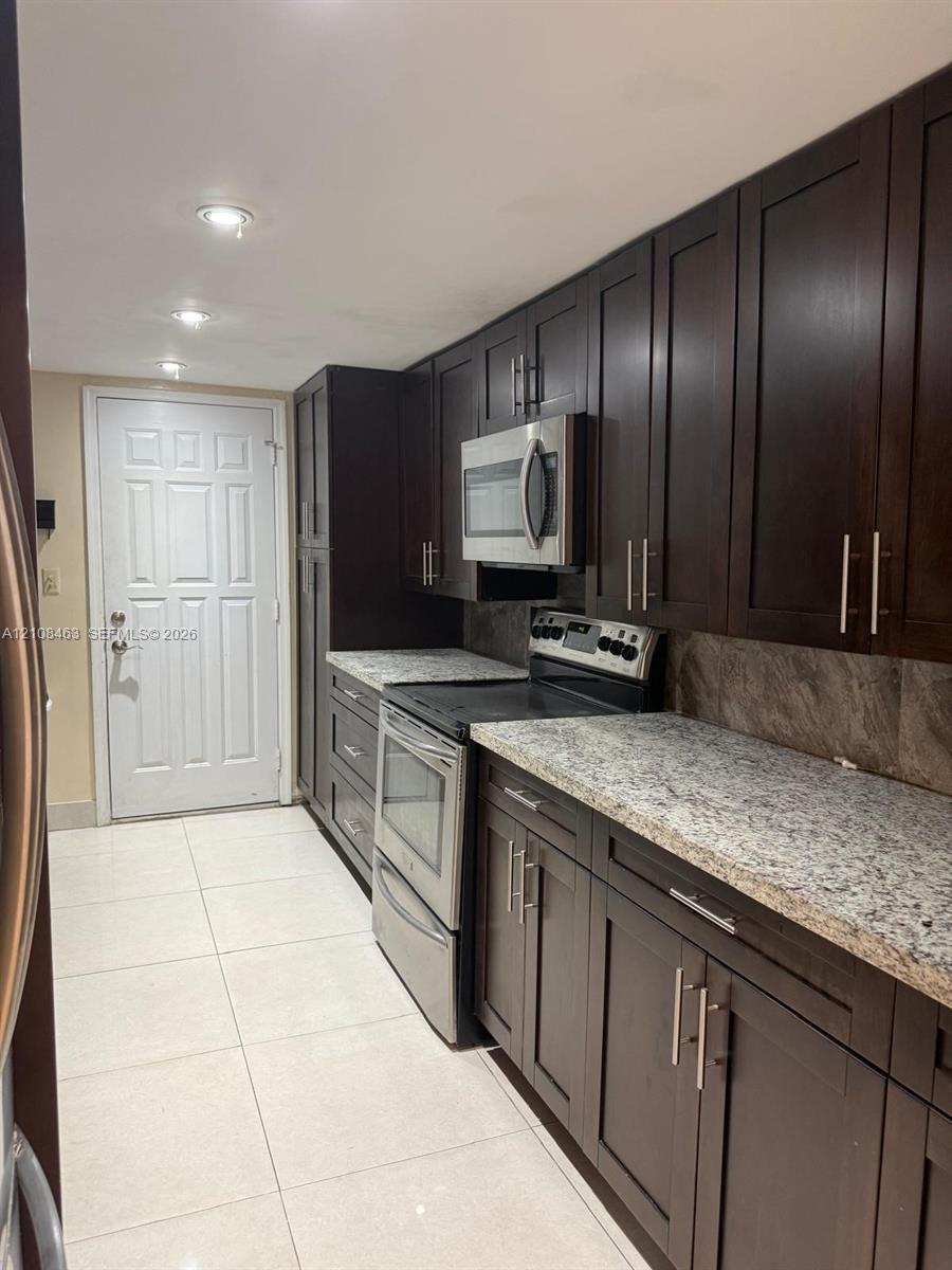 Dark wood-finish cabinetry, stone-finish countertops, stainless steel appliances, tile flooring, and recessed lighting Dark wood-finish cabinetry, stone-finish countertops, stainless steel appliances, tile flooring, and recessed lighting