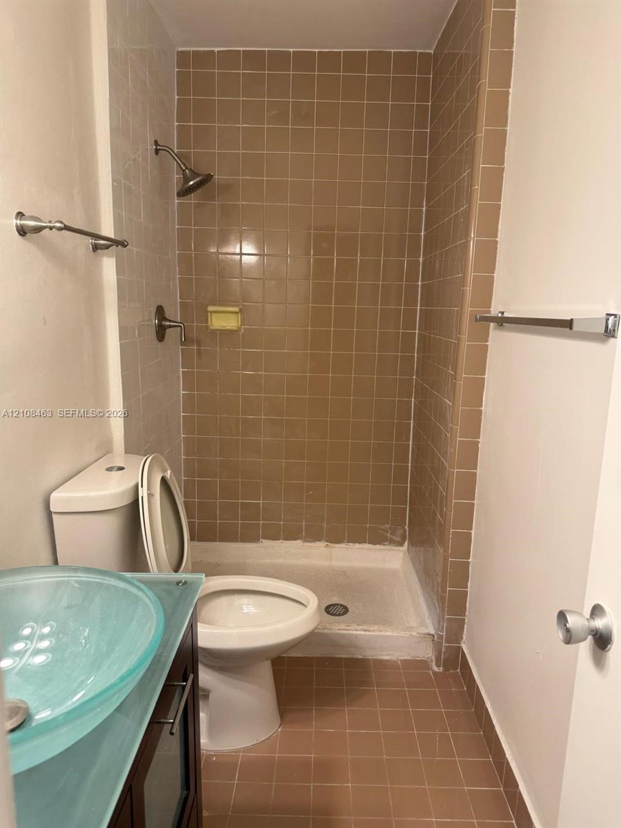 Bathroom featuring a glass vessel sink, dark-toned cabinetry, walk-in shower stall with tiled surround, and tiled flooring