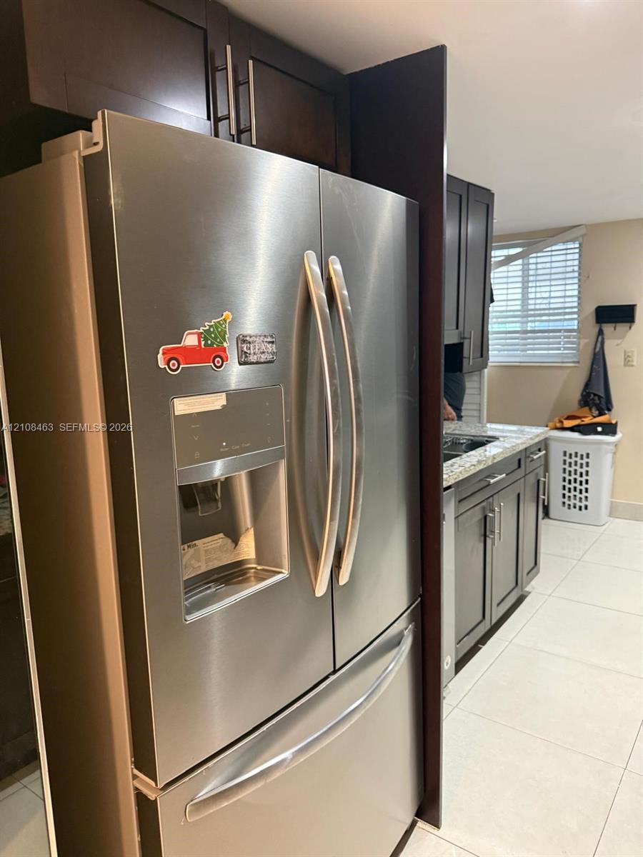 Stainless steel French-door refrigerator, dark-finish cabinetry with silver-tone hardware, stone-composite countertops, and tile flooring Stainless steel French-door refrigerator, dark-finish cabinetry with silver-tone hardware, stone-composite countertops, and tile flooring
