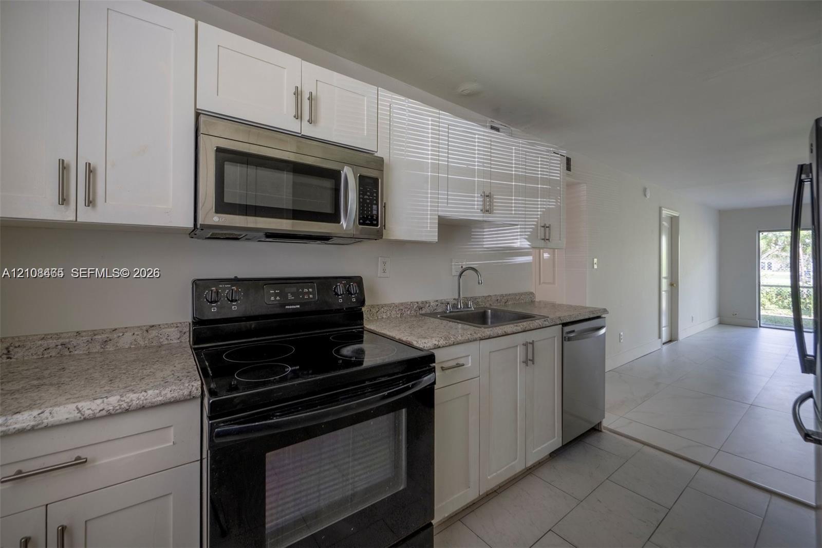 Kitchen featuring white shaker-style cabinetry, stone countertops, stainless steel microwave, black electric range, and tile flooring