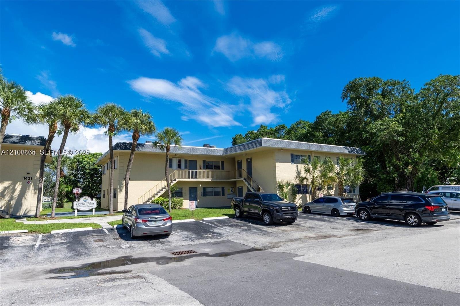 Multi-level exterior featuring a painted stucco facade, external metal staircases, paved surface parking, and mature palm trees