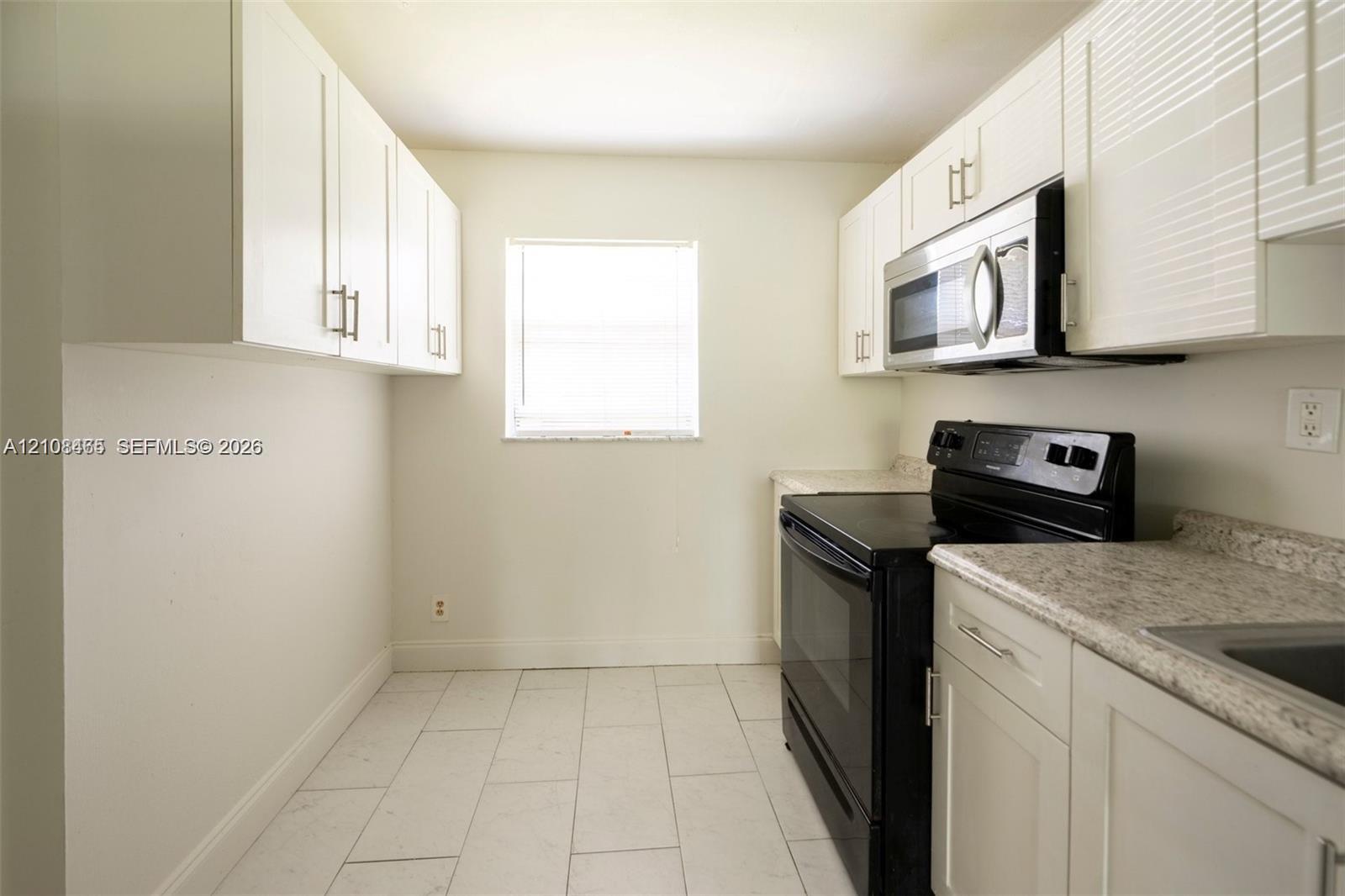 Kitchen featuring white cabinetry, stone-finish countertops, black appliances including a range and over-the-range microwave, and tile flooring