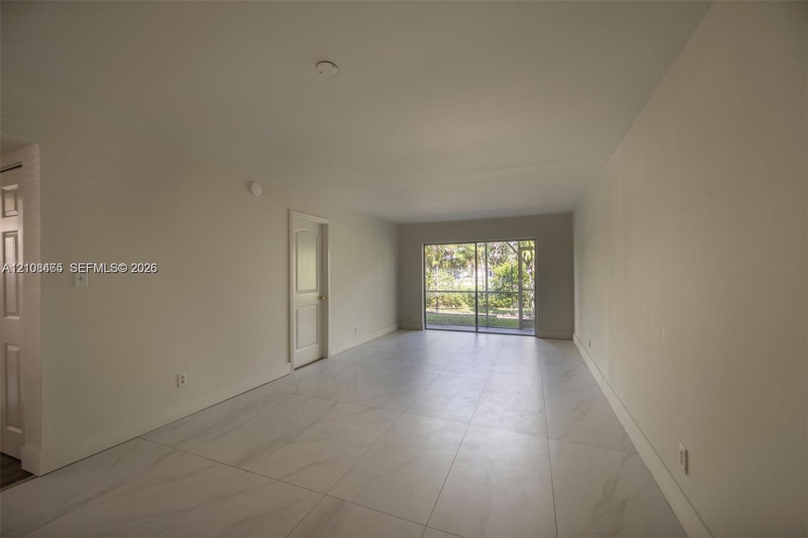 Large-format tile flooring, neutral walls, and a multi-panel sliding glass door leading to a screened enclosure