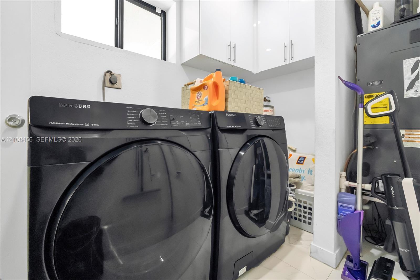 Dedicated utility area featuring white shaker-style cabinetry with brushed nickel hardware and a window for natural light