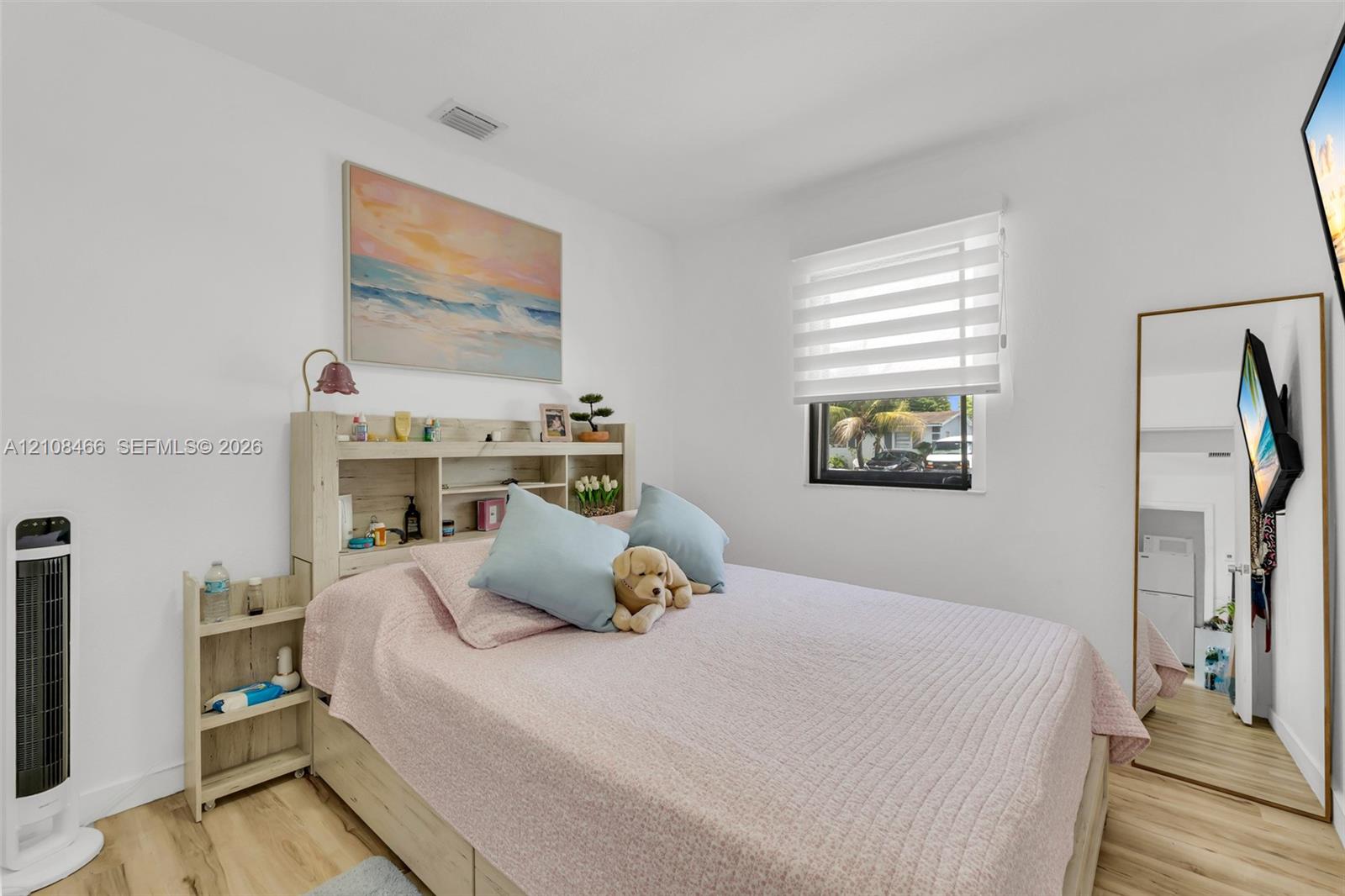 Neutral-toned wood-finish flooring, white walls, and a window featuring adjustable horizontal blinds