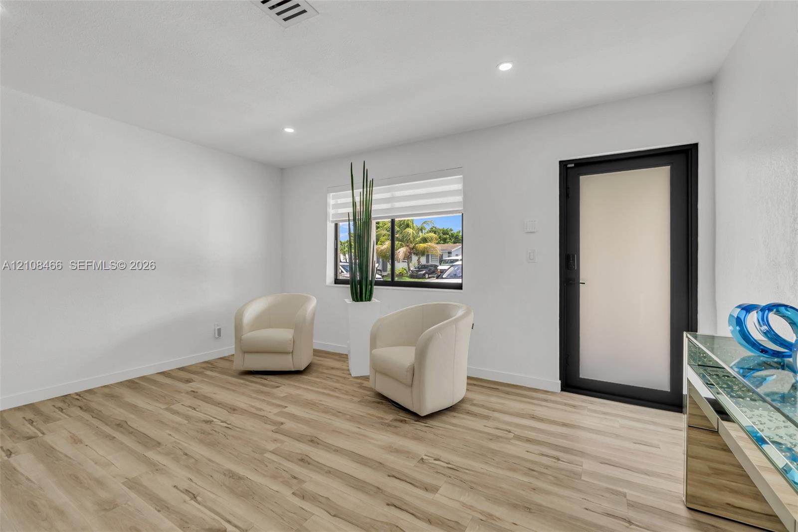 Interior space featuring wood-finish flooring, recessed lighting, a window with horizontal blinds, and a door with a frosted glass panel and black trim Interior space featuring wood-finish flooring, recessed lighting, a window with horizontal blinds, and a door with a frosted glass panel and black trim