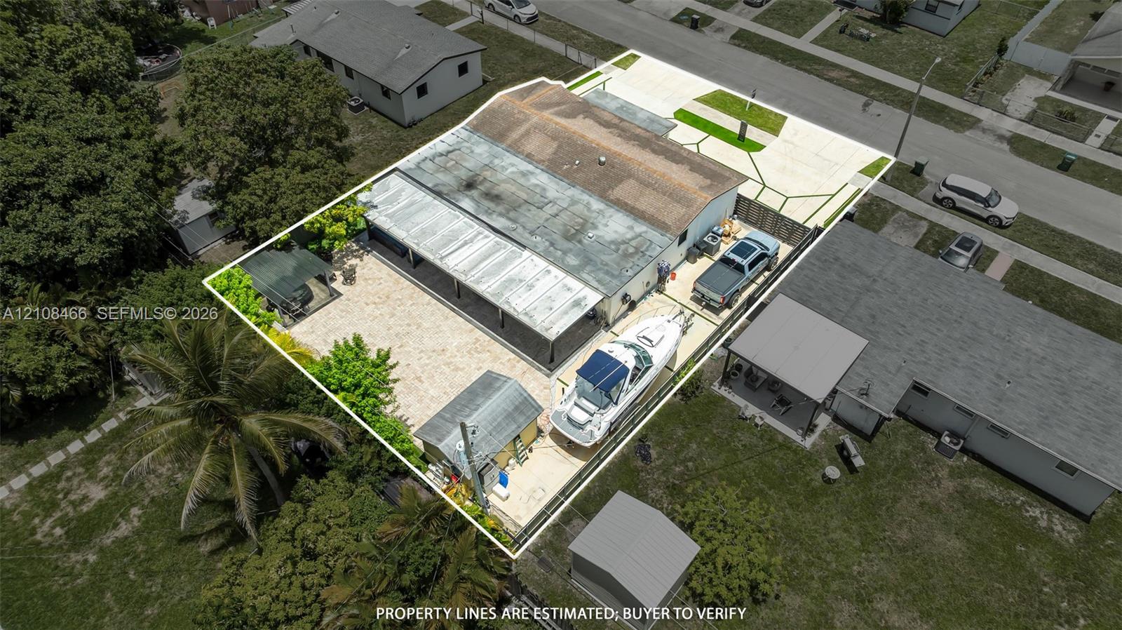 Aerial perspective of residential property featuring a concrete driveway, gated gravel parking area, metal-covered patio, and a detached storage structure