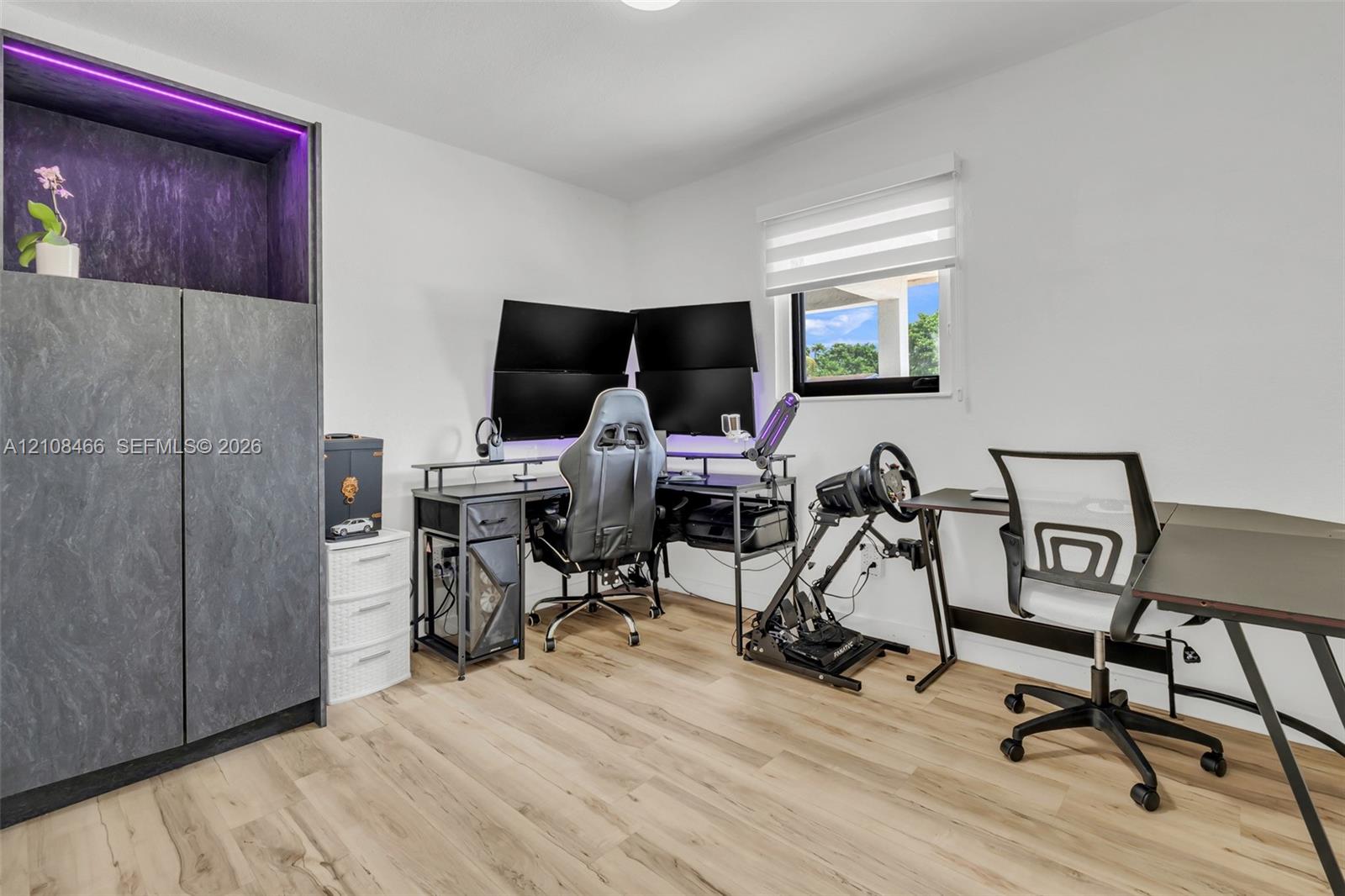 Room featuring wood-finish flooring, a built-in floor-to-ceiling cabinet with integrated accent lighting, and a window with horizontal roller shades
