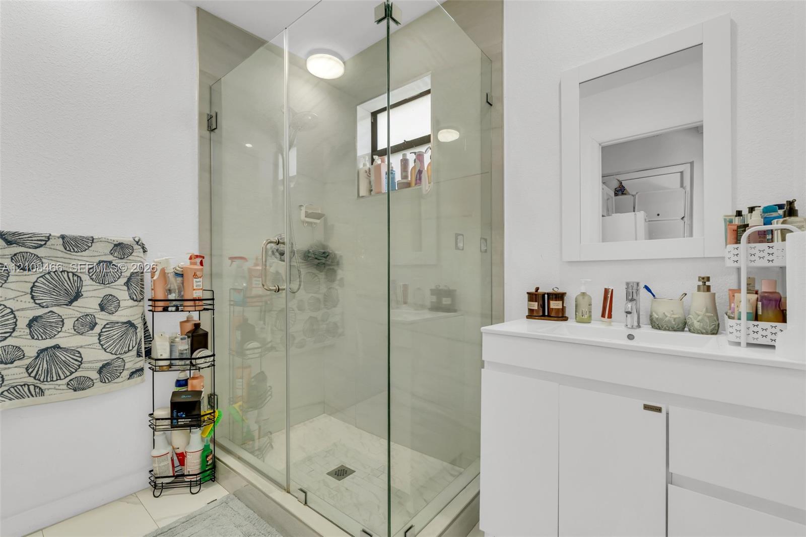 Frameless glass shower enclosure with tiled walls, white vanity featuring an integrated sink, and a wall-mounted framed mirror