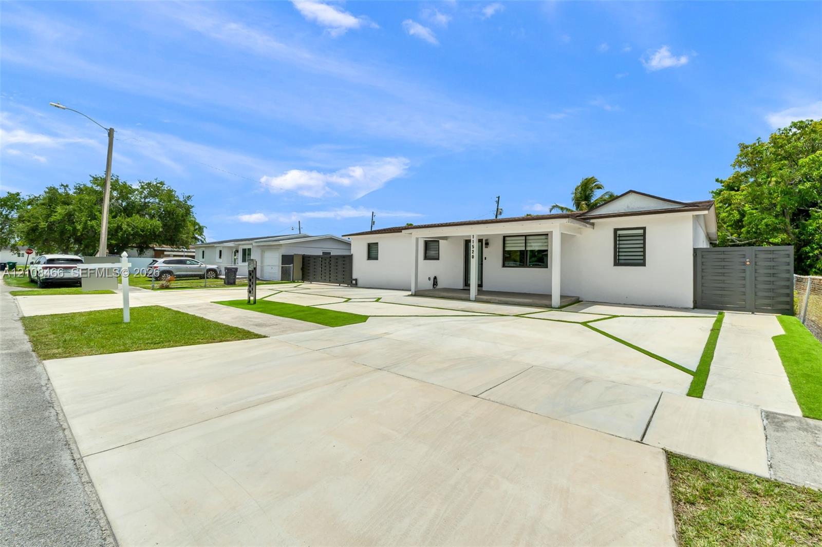 Single-story residence featuring a smooth stucco exterior, a geometric concrete driveway with turf-accented inlay, a covered front entryway, and privacy-focused perimeter fencing Single-story residence featuring a smooth stucco exterior, a geometric concrete driveway with turf-accented inlay, a covered front entryway, and privacy-focused perimeter fencing