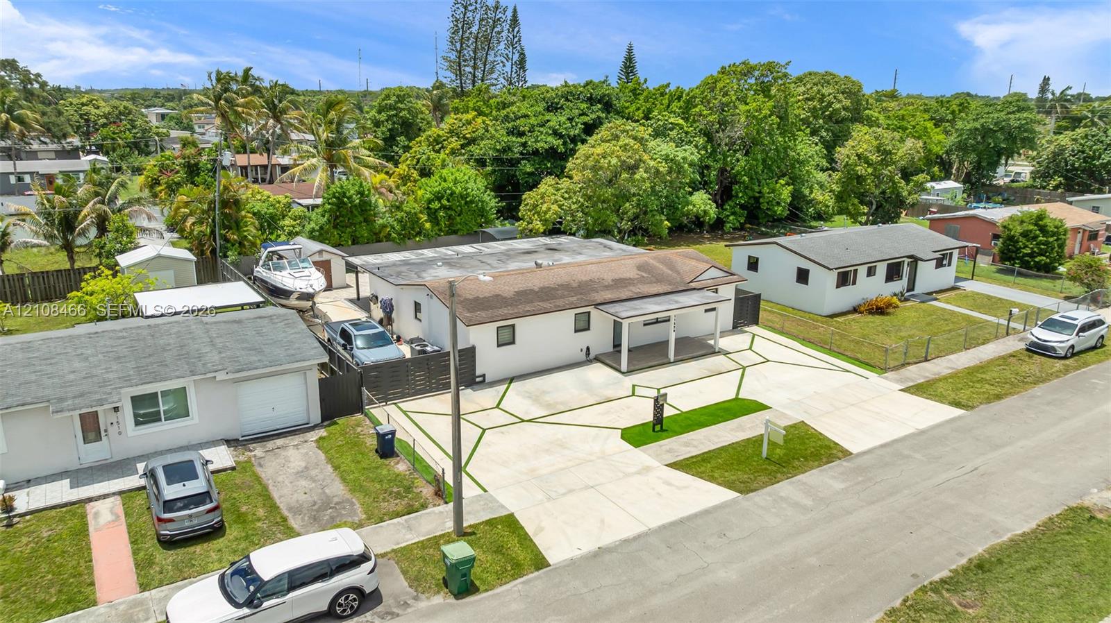 Single-story residence featuring a concrete exterior, covered front porch, custom geometric-pattern concrete driveway with inset grass turf, and enclosed outdoor storage areas