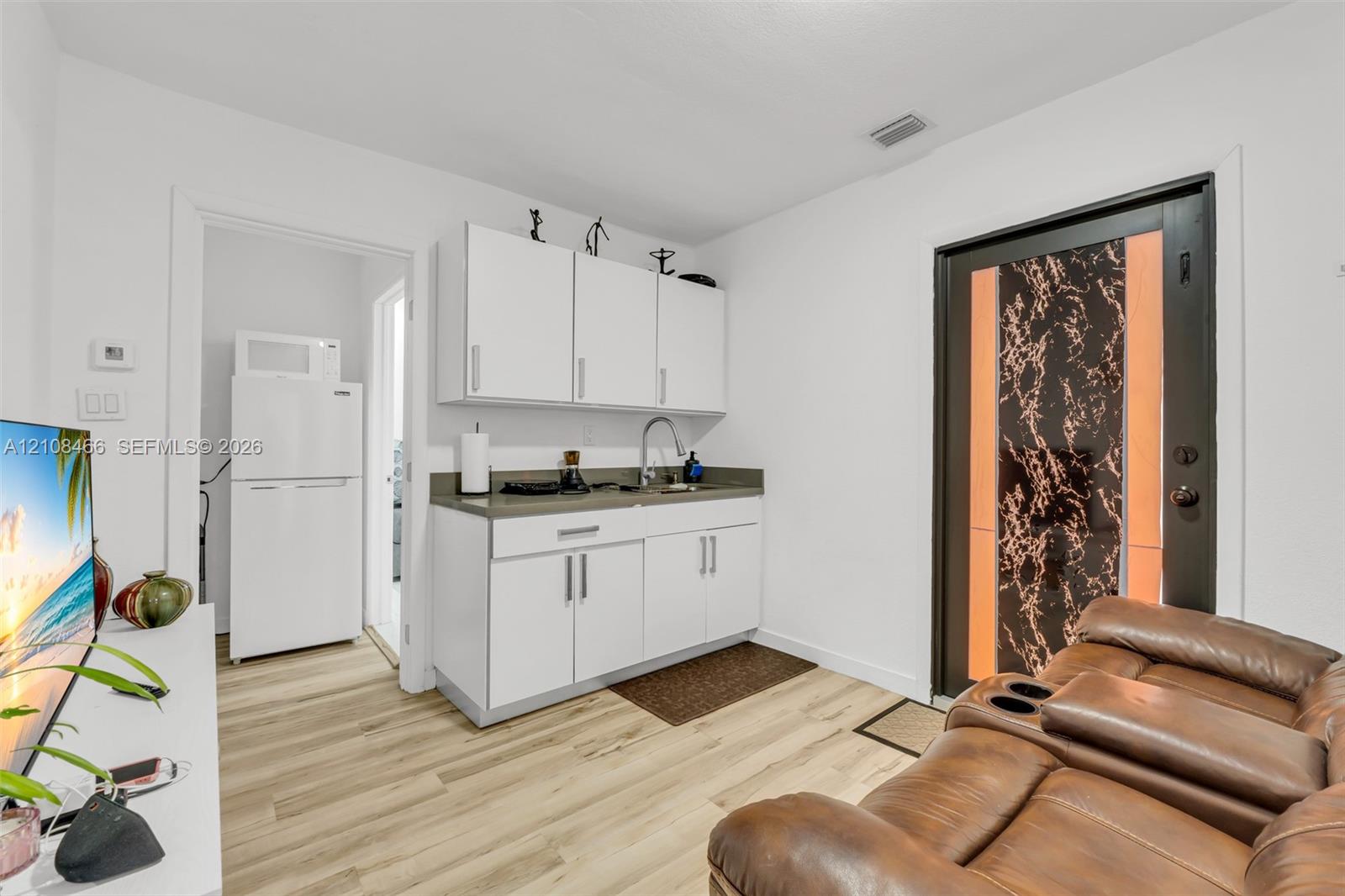 Kitchenette featuring white cabinetry, a sink with a metal faucet, solid-surface countertops, and wood-finish flooring, accented by an exterior door with a patterned glass insert
