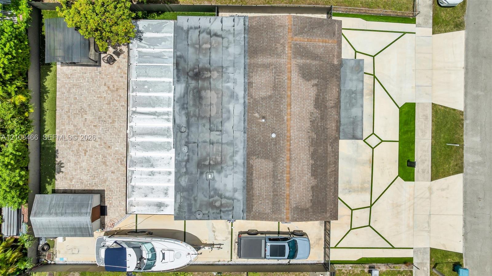 Aerial perspective featuring a multi-section roof, a geometric concrete paved driveway, a gravel backyard area, and a detached storage structure