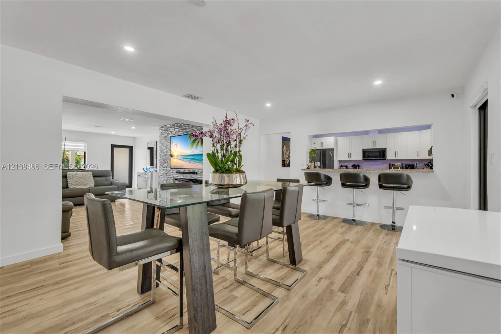 Open-concept area featuring wood-finish flooring, recessed lighting, white cabinetry, stone-surfaced breakfast bar, and a stone-clad accent wall