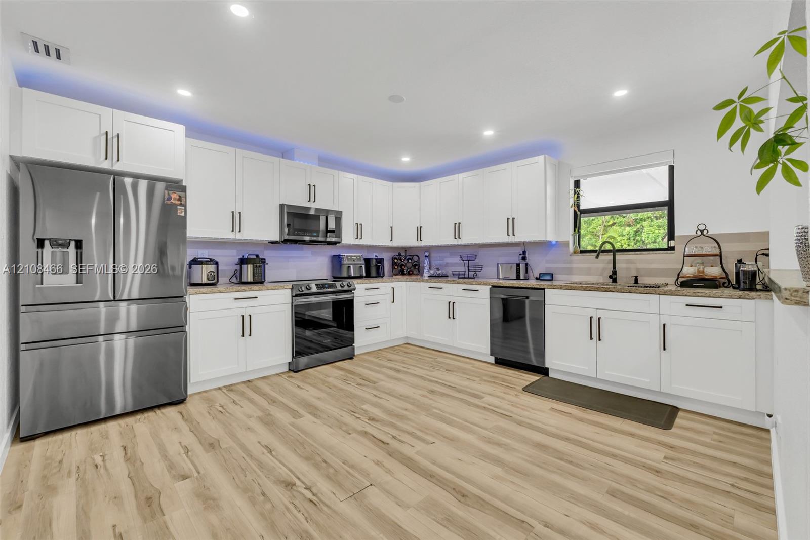 Kitchen featuring white shaker cabinetry, stainless steel appliances, stone-finish countertops, recessed lighting, and wood-finish flooring