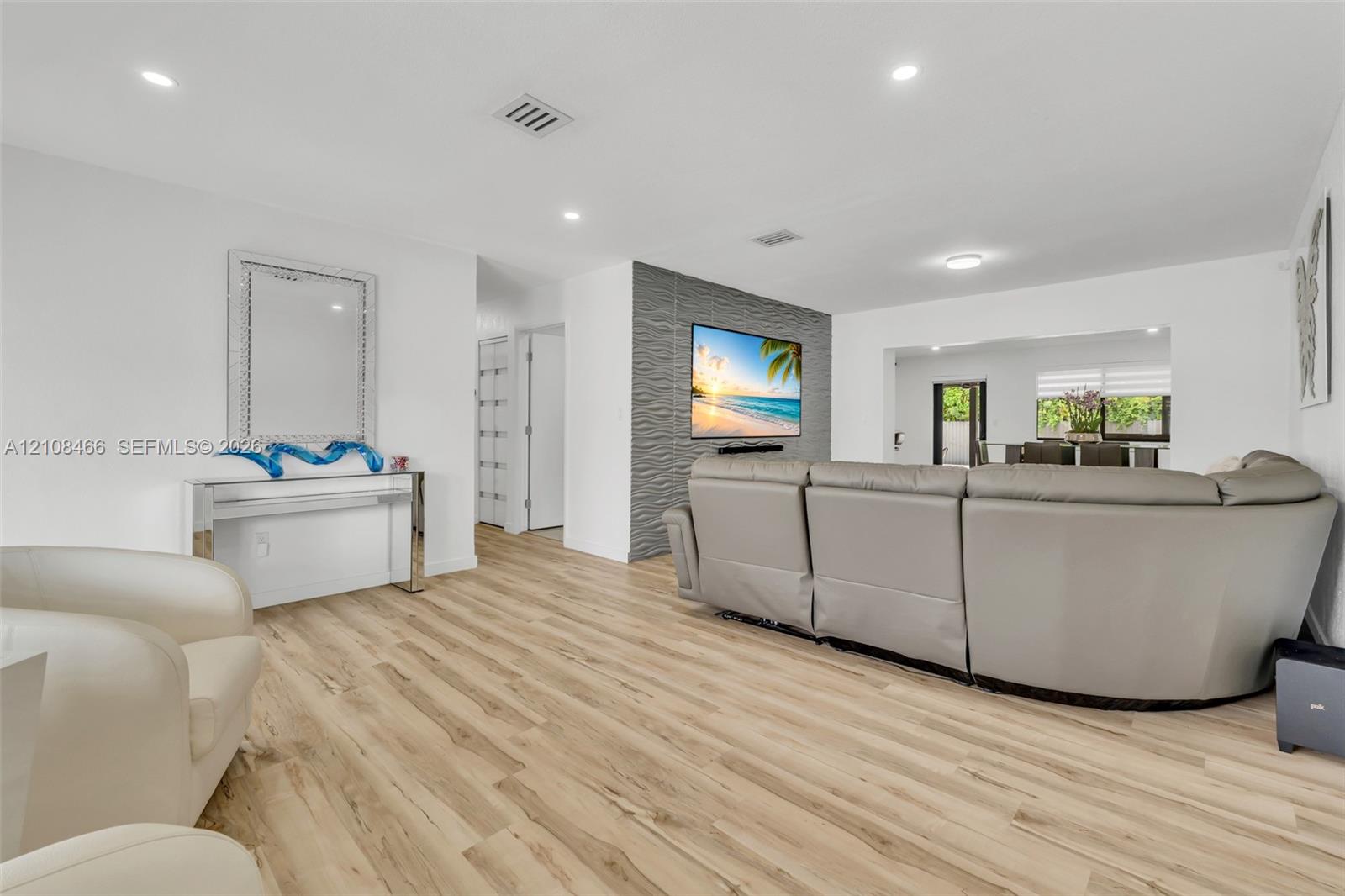 Living area featuring wood-finish flooring, recessed lighting, and a grey textured accent wall Living area featuring wood-finish flooring, recessed lighting, and a grey textured accent wall