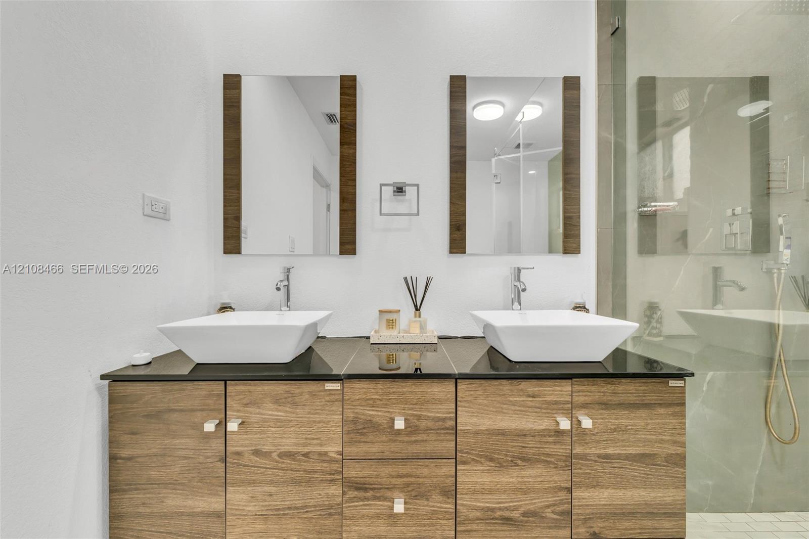 Dual-sink vanity featuring wood-finish cabinetry, a dark solid-surface countertop, rectangular vessel sinks, and rectangular wall-mounted mirrors with wood-finish frames