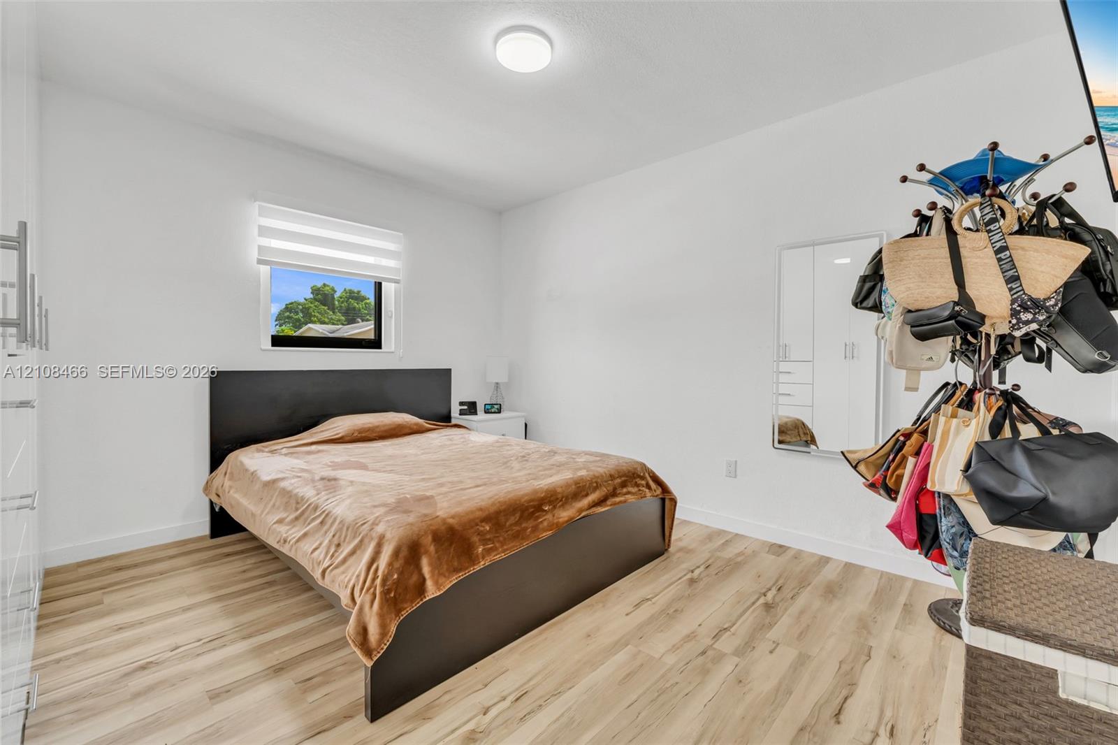 Room featuring wood-finish flooring, a recessed window with an integrated blind, and a white-framed built-in mirror