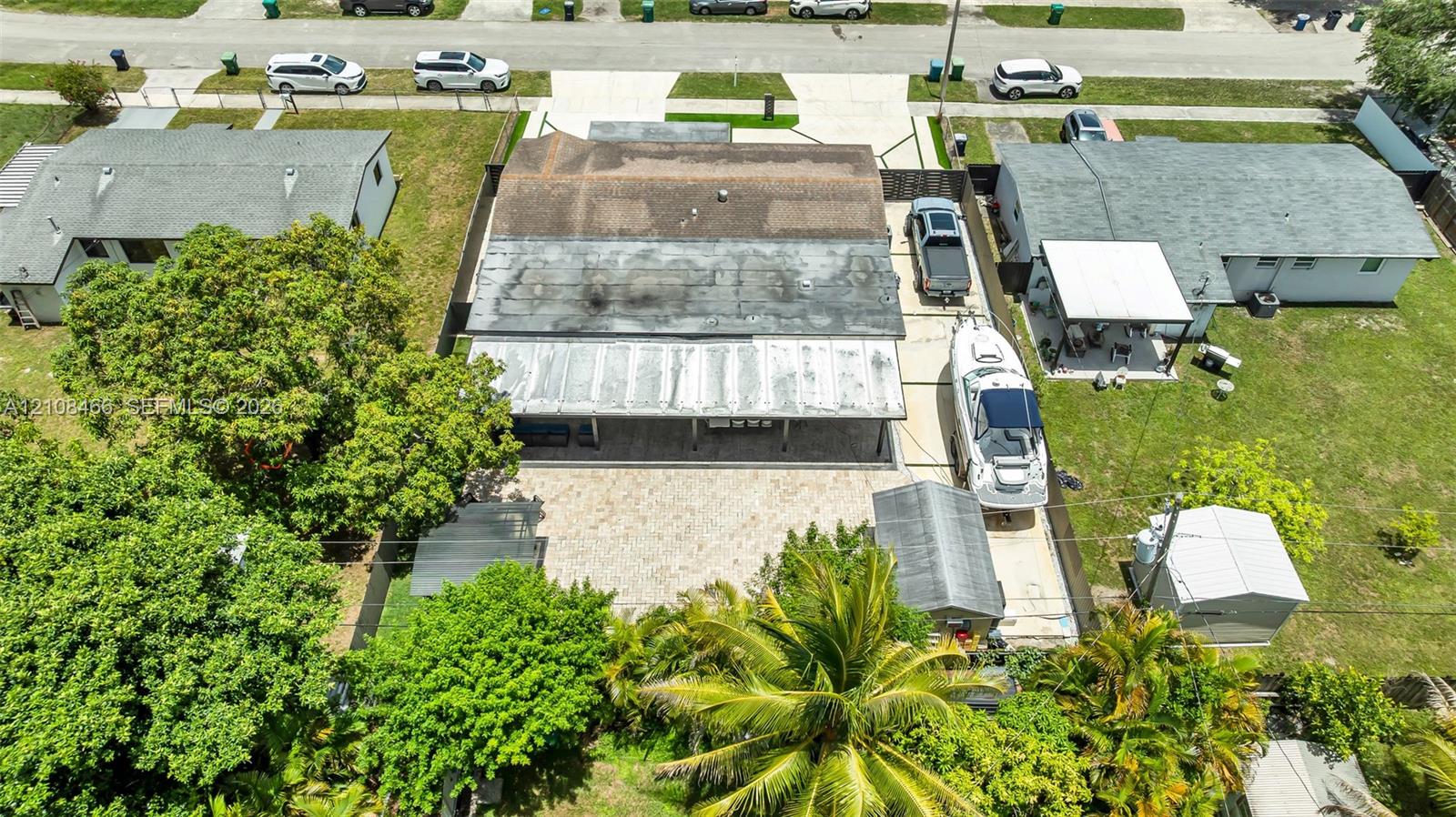 Aerial perspective of property featuring a paved driveway, concrete hardscaping, attached covered rear patio, mature trees, and detached storage shed