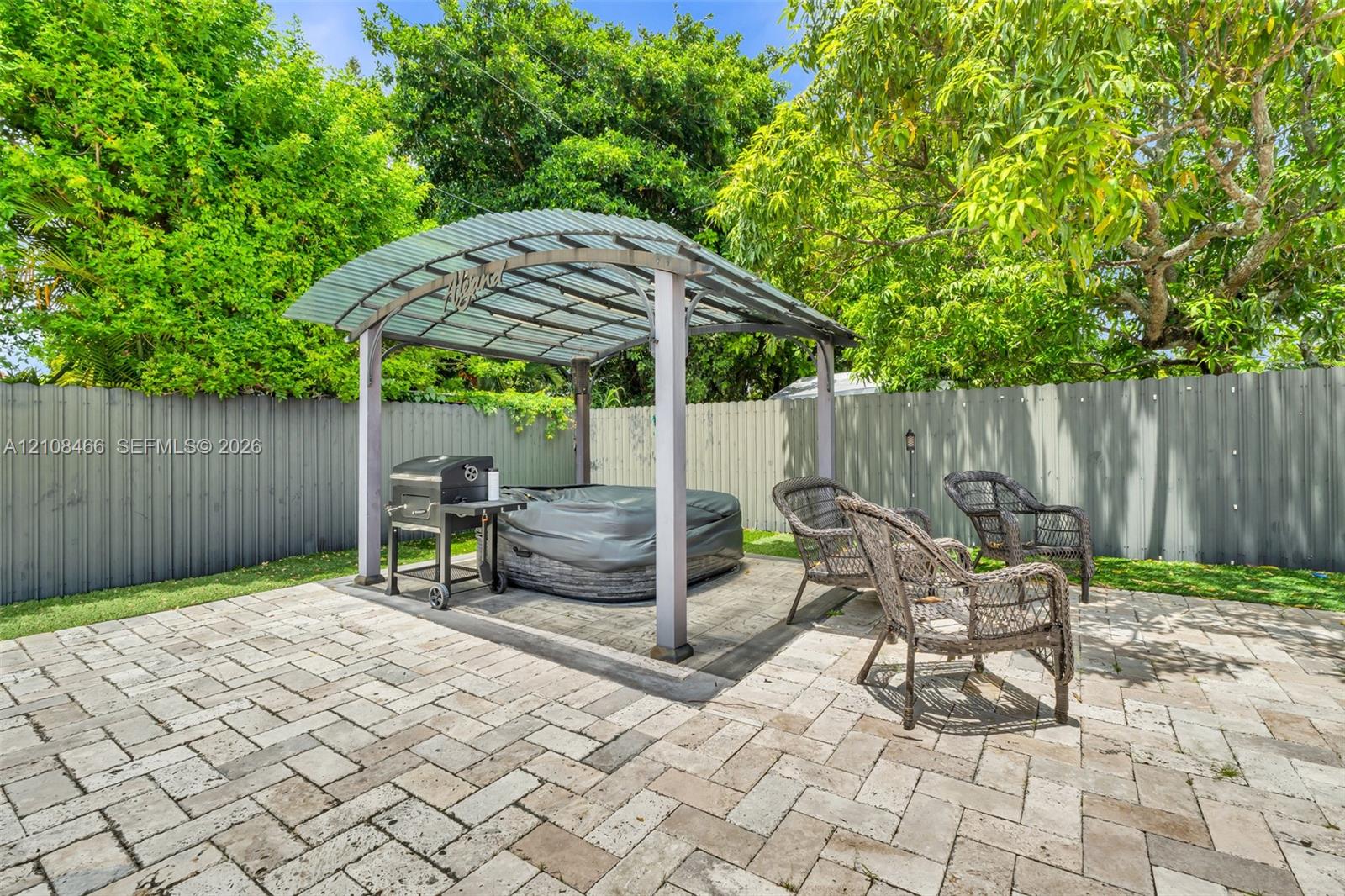 Herringbone-patterned stone paver patio featuring a metal-framed gazebo, privacy fencing, and mature landscaping