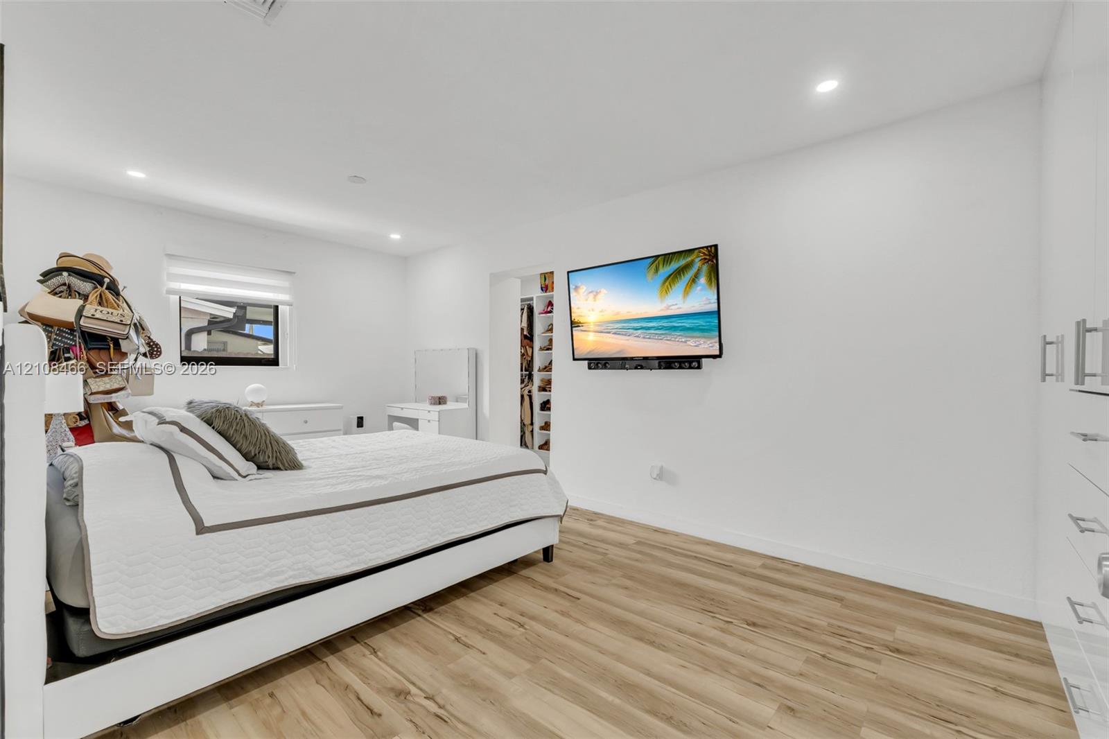Neutral-toned room featuring wood-finish flooring, recessed lighting, white wall-mounted cabinetry, and a reach-in closet with integrated shelving