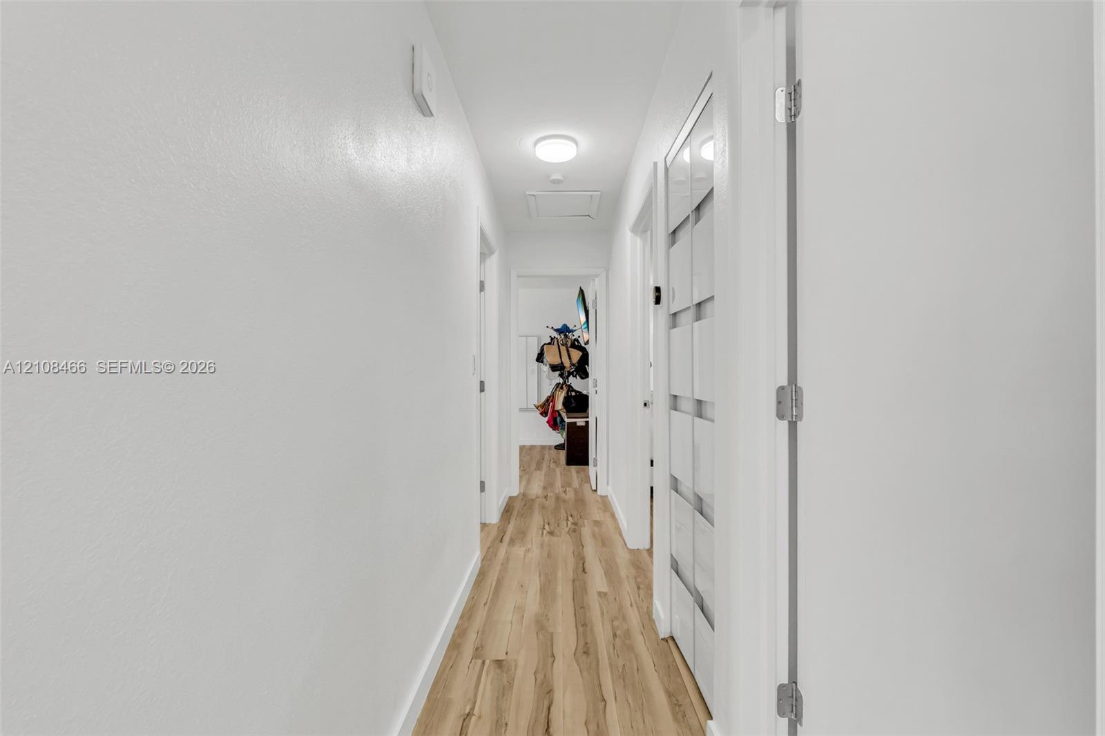 Hallway featuring wood-finish flooring, white walls, flush-mount ceiling lighting, and a multi-panel door with glass inserts