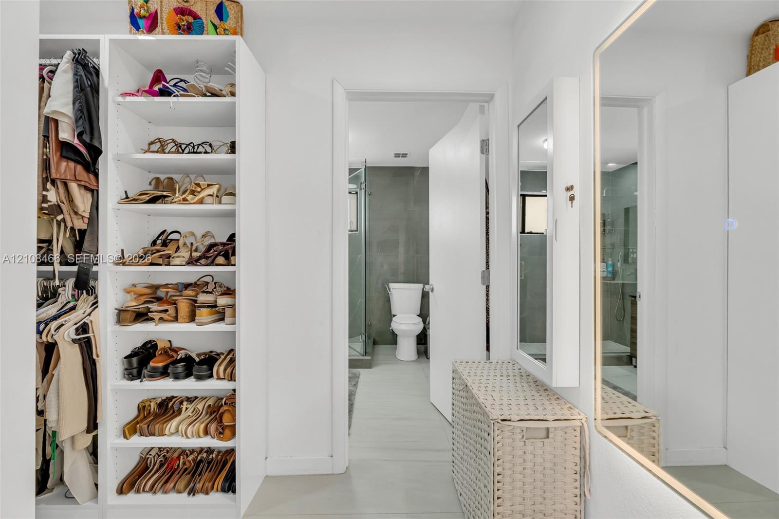 Custom walk-in closet featuring floor-to-ceiling built-in white shelving, integrated hanging rods, and a large wall-mounted mirror