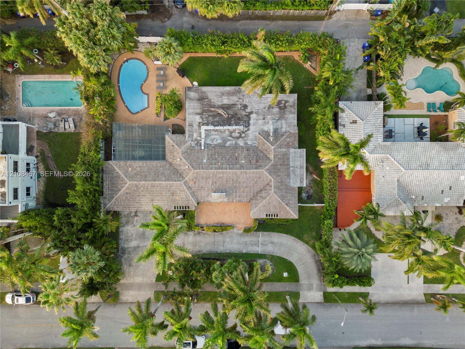 Aerial perspective of a property featuring an in-ground swimming pool, a screened-in patio area, a concrete driveway, and mature landscaping