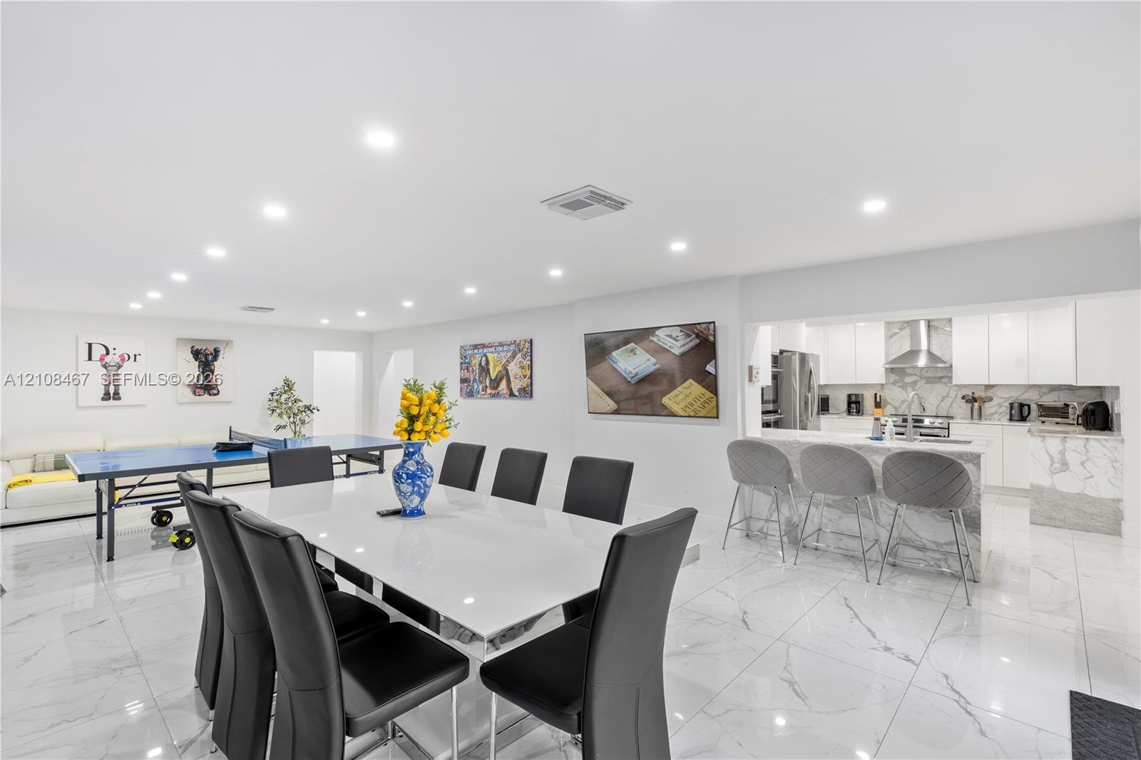 Large-format tile flooring, recessed ceiling lighting, and a kitchen featuring a stone-finish waterfall edge peninsula, white cabinetry, and stainless steel range hood