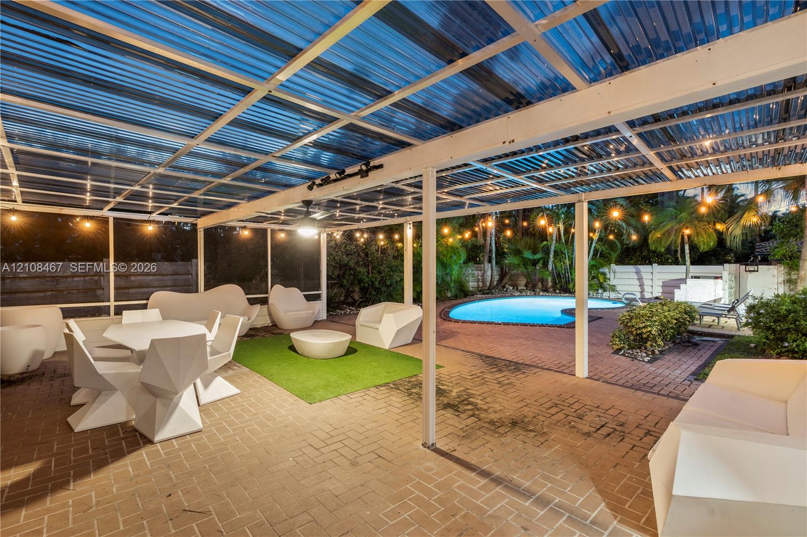 Screened-in outdoor patio with corrugated translucent roofing, brick paver flooring, attached track lighting, and a kidney-shaped swimming pool