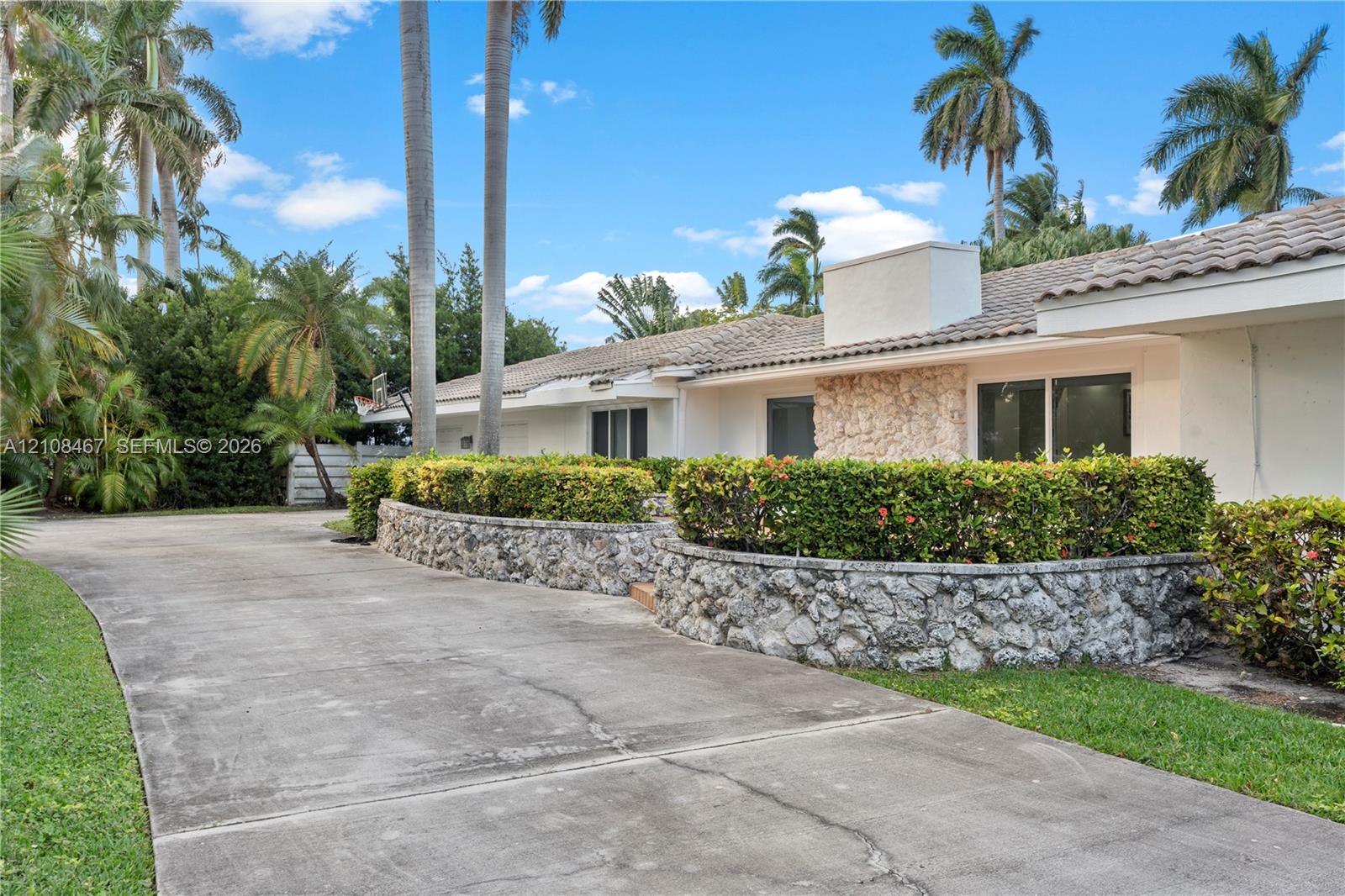 Single-story residence featuring a concrete driveway, stone-veneer exterior accents, tile roof, and terraced landscaping with stone retaining walls Single-story residence featuring a concrete driveway, stone-veneer exterior accents, tile roof, and terraced landscaping with stone retaining walls