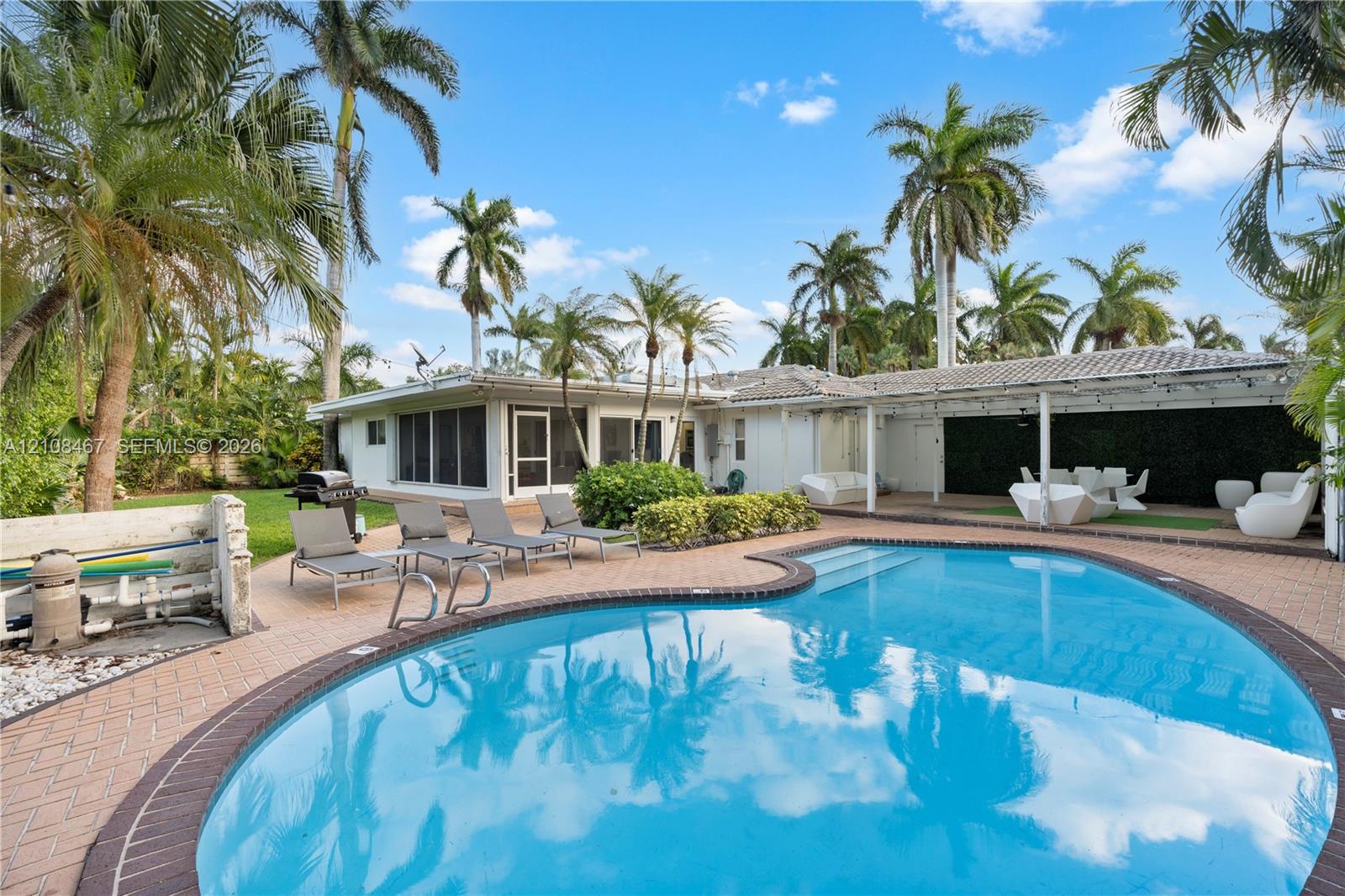 Free-form swimming pool with brick coping, expansive paved patio, screened-in enclosure, and lush landscaping featuring mature palm trees